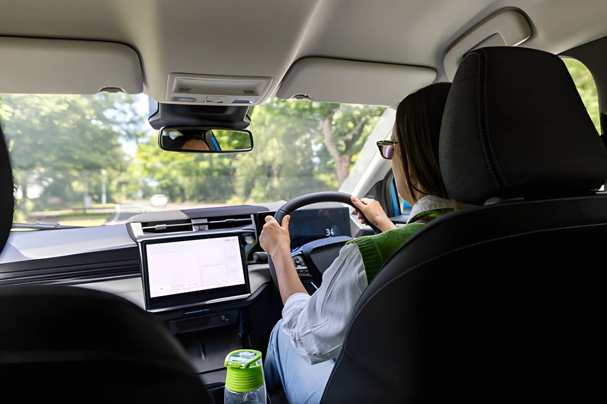 Seen from the back seat, a driver keeps both hands on the steering wheel of a right-hand-drive car on a tree-lined road.