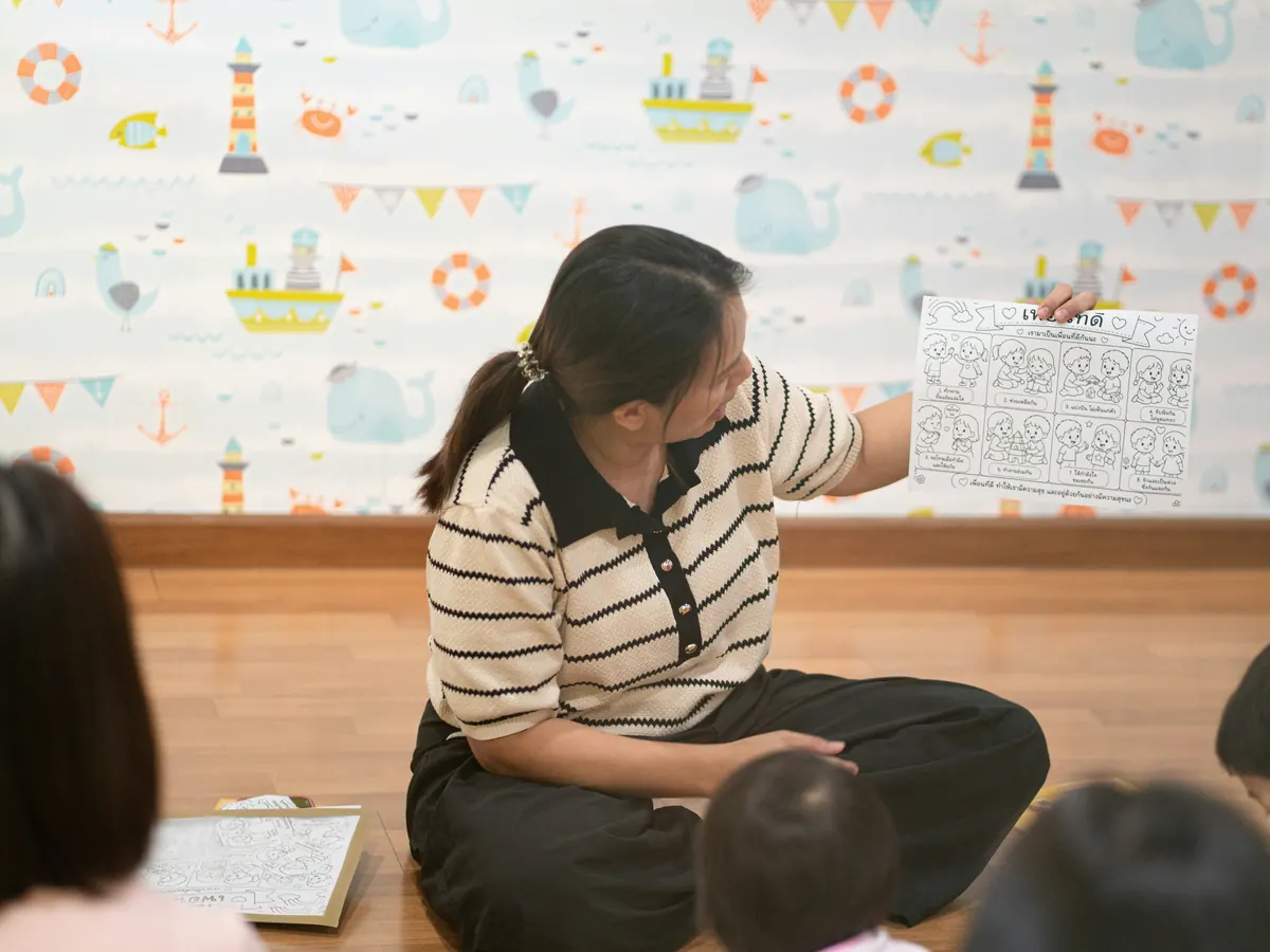 An educator reading and showing a picture to children seated on the floor