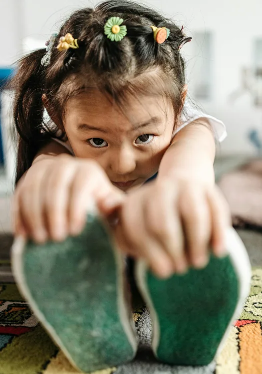A child holding up two large green leaves outdoors