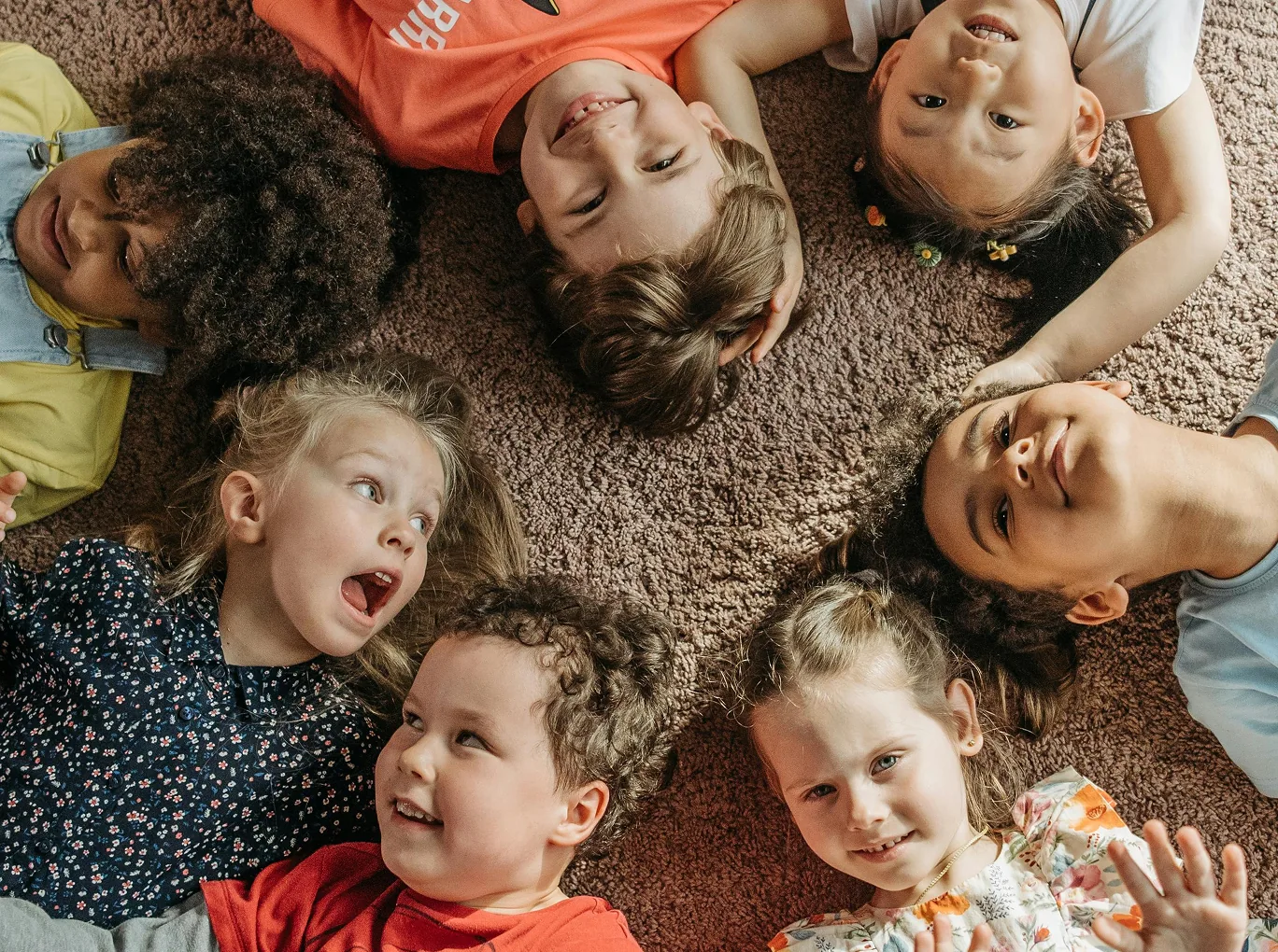 Children lying in a circle on a rug, laughing together