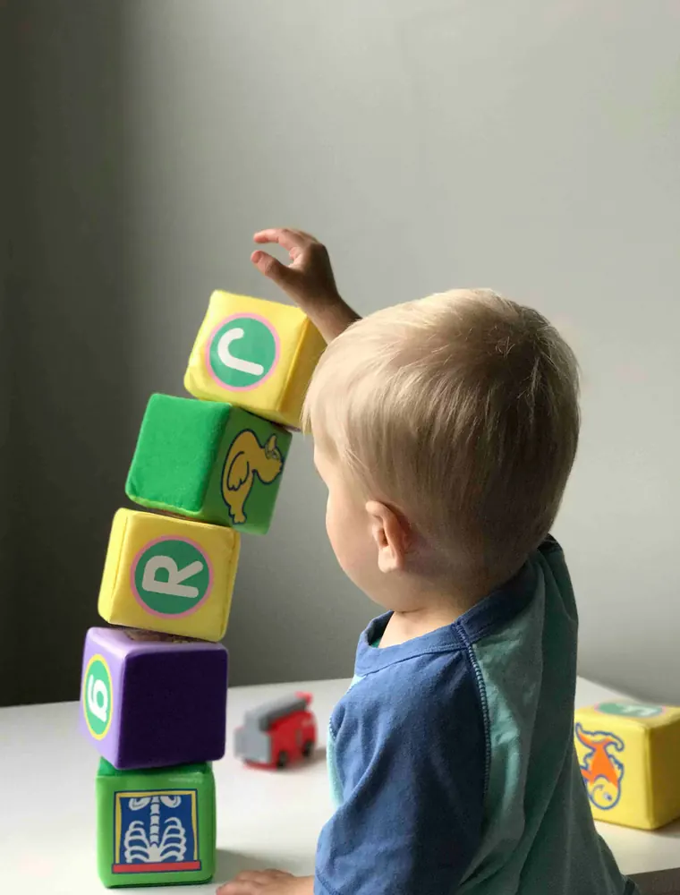 A child carefully stacking wooden alphabet blocks into a tower
